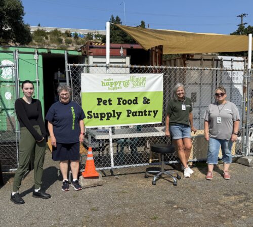 Four people standing in front of a sign for the shelter's Pet Food & Supply Pantry.